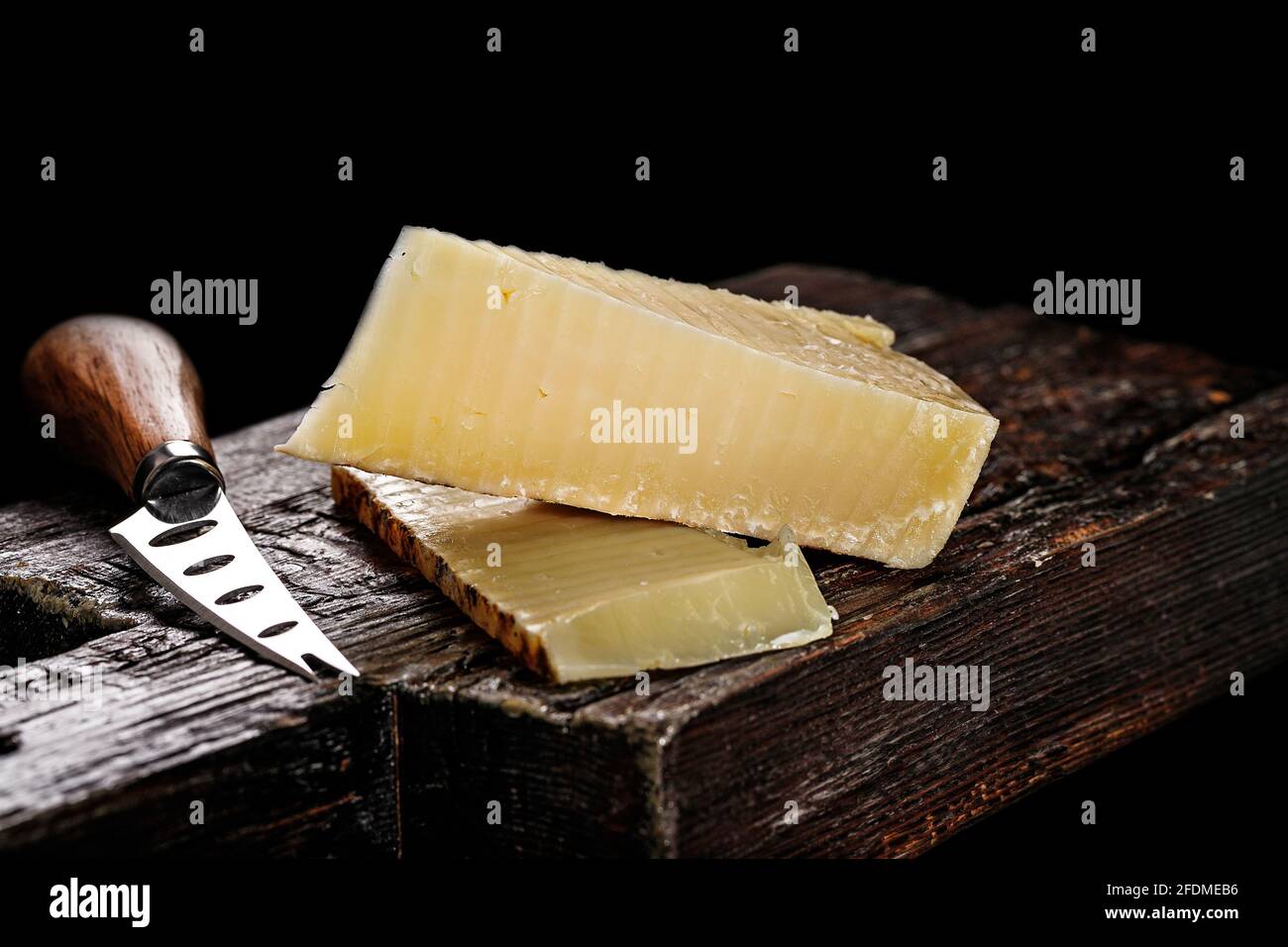 Primo piano di formaggio Cheddar. Formaggio di vacca invecchiato semi-morbido secondo una vecchia ricetta inglese. Pezzo di formaggio su una tavola di legno scuro e coltello per Foto Stock