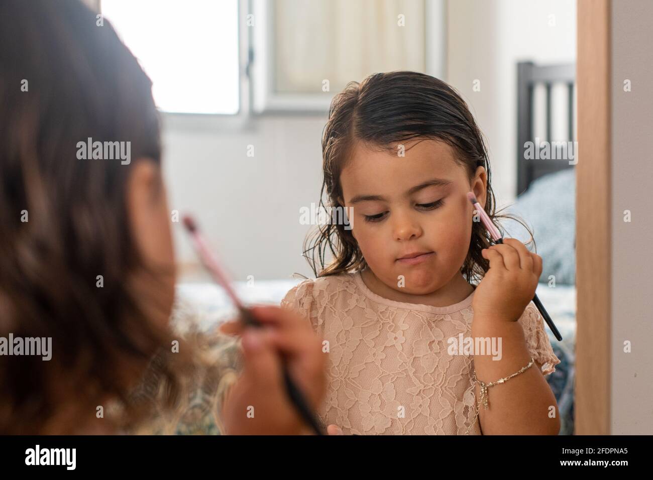 Una piccola ragazza caucasica, vestita con un bel vestito, che si sta facendo il trucco con il pennello di sua madre, di fronte allo specchio nell'ro dei suoi genitori Foto Stock