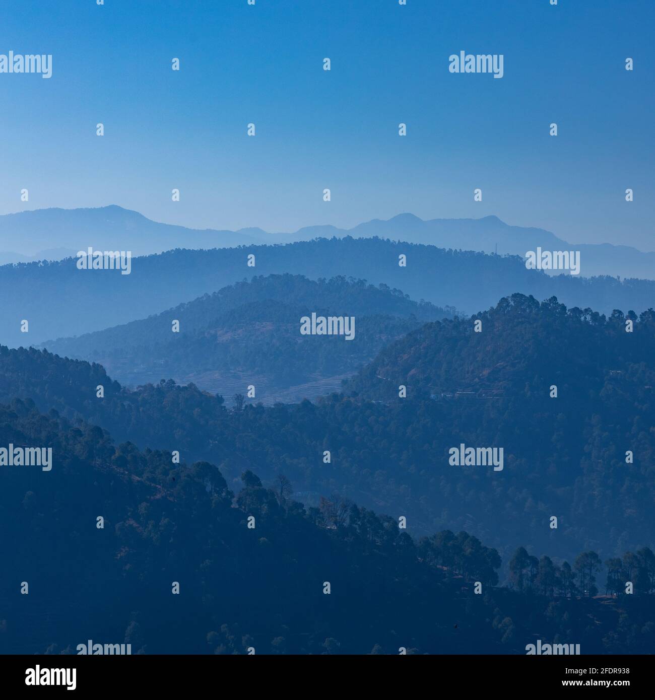 Vista delle silhouette di montagna con alberi e nebbia e chiaro cielo blu Foto Stock