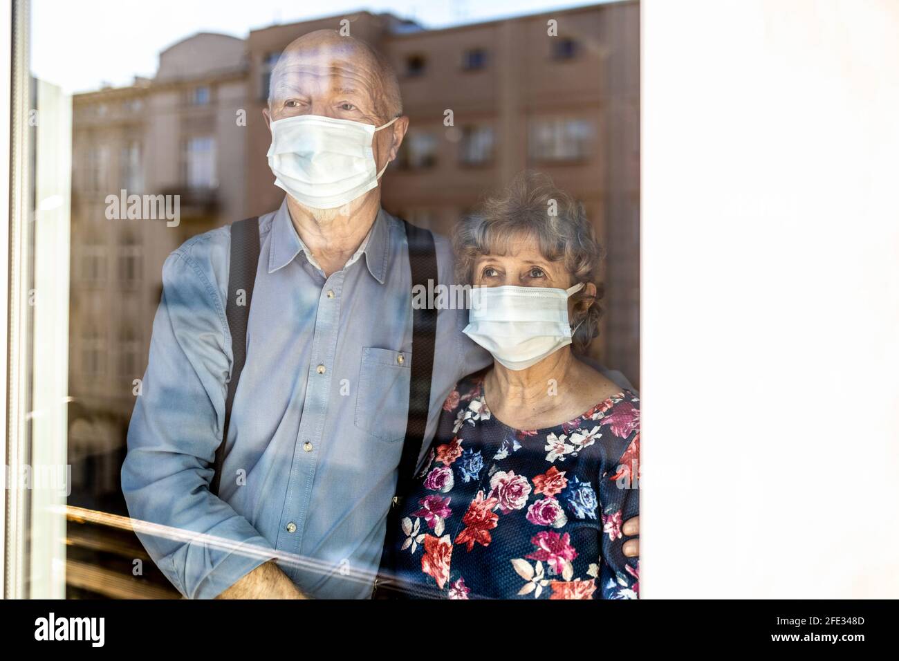 Coppia anziana preoccupata che guarda attraverso la finestra a casa durante il coronavirus COVID-19 epidemia Foto Stock