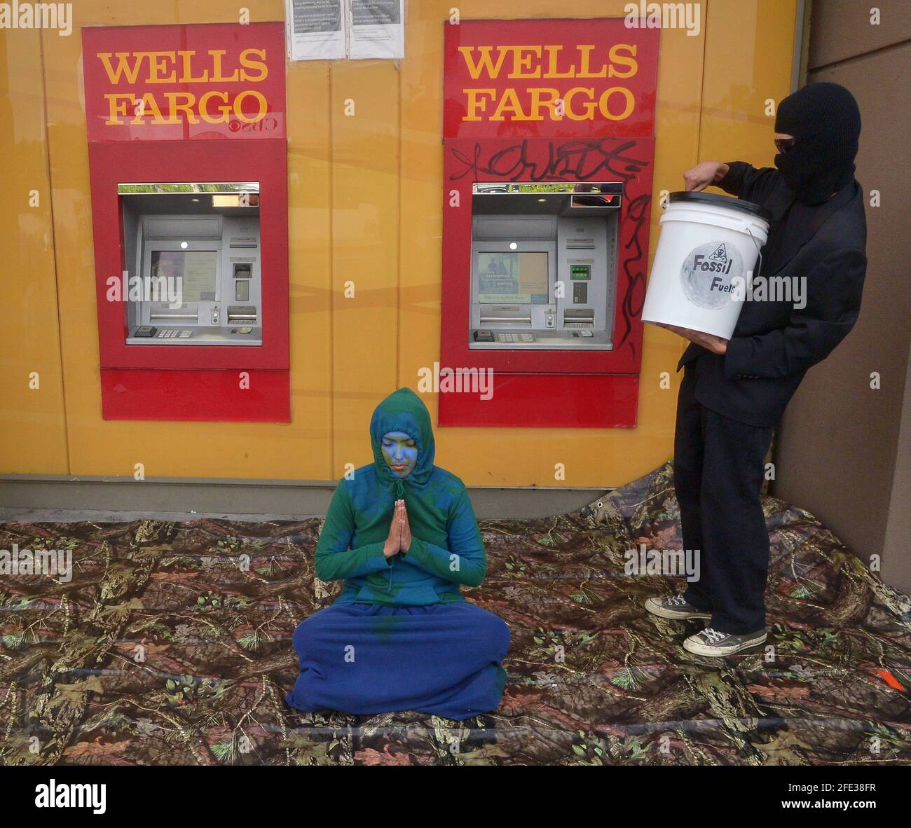 Un protester si prepara a versare sangue simulato su un altro protestore di fronte a un ATM come parte di un 'grievance Gathering' per chiedere che Wells Fargo 'ritrae immediatamente il suo investimento nel progetto di oleodotto di sabbie bituminose della linea 3 di Enbridge' presso una filiale della banca Wells Fargo nell'area di Fairfax di Los Angeles venerdì 23 aprile 2021. I dimostranti sostengono che il progetto accrescirebbe il rischio di una "catastrofe ambientale" e disonorerebbe i "trattati indigeni". Wells Fargo è uno dei più grandi banchieri di progetti di combustibili fossili del mondo. Foto di Jim Ruymen Foto Stock