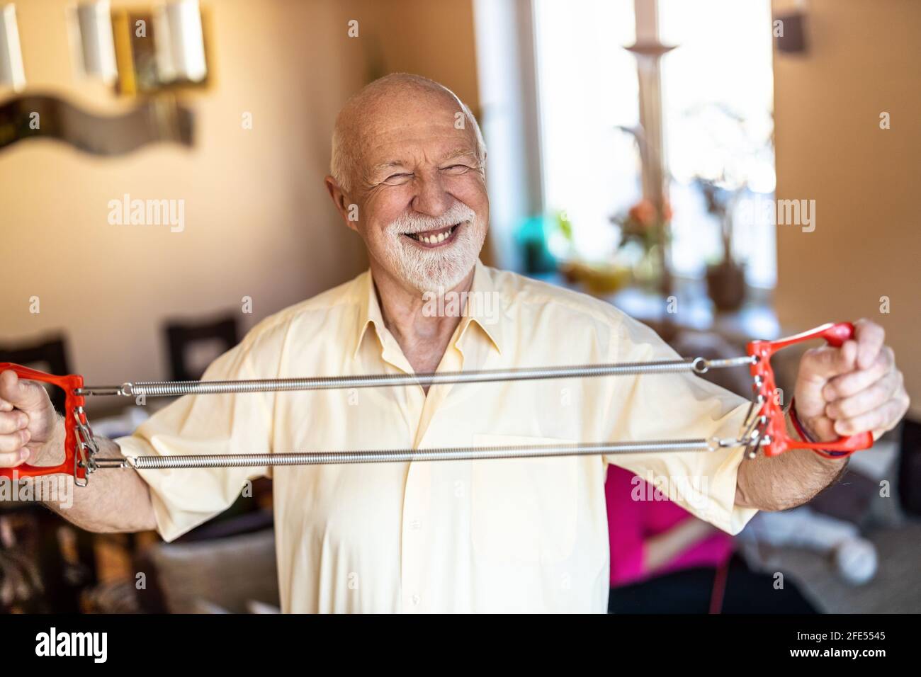 Uomo anziano che si esercita usando l'espansore del petto in soggiorno Foto Stock