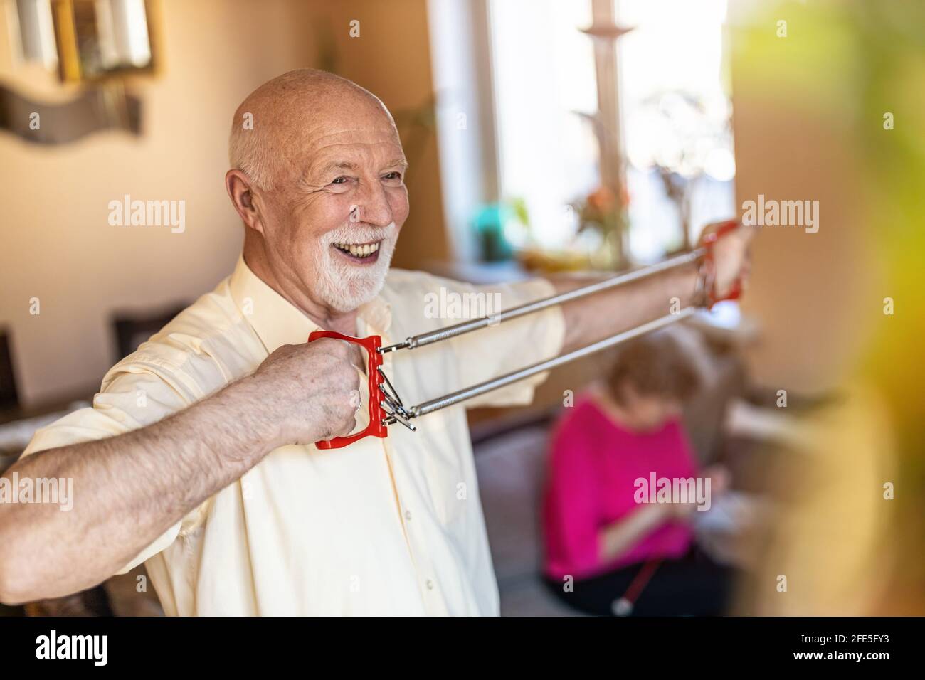 Uomo anziano che si esercita usando l'espansore del petto in soggiorno Foto Stock