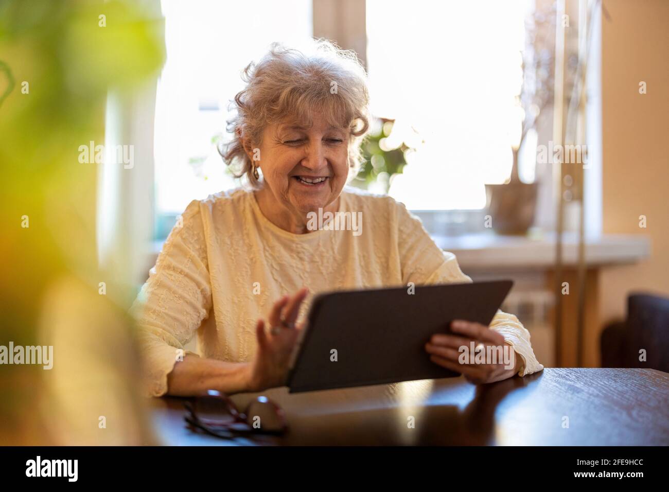 Una donna anziana felice che usa un tablet digitale a casa Foto Stock