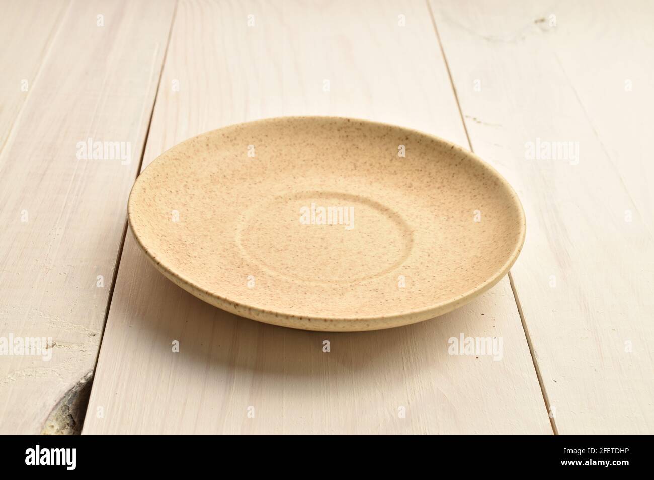Piatto in ceramica marrone chiaro, primo piano, su un tavolo dipinto di bianco. Foto Stock