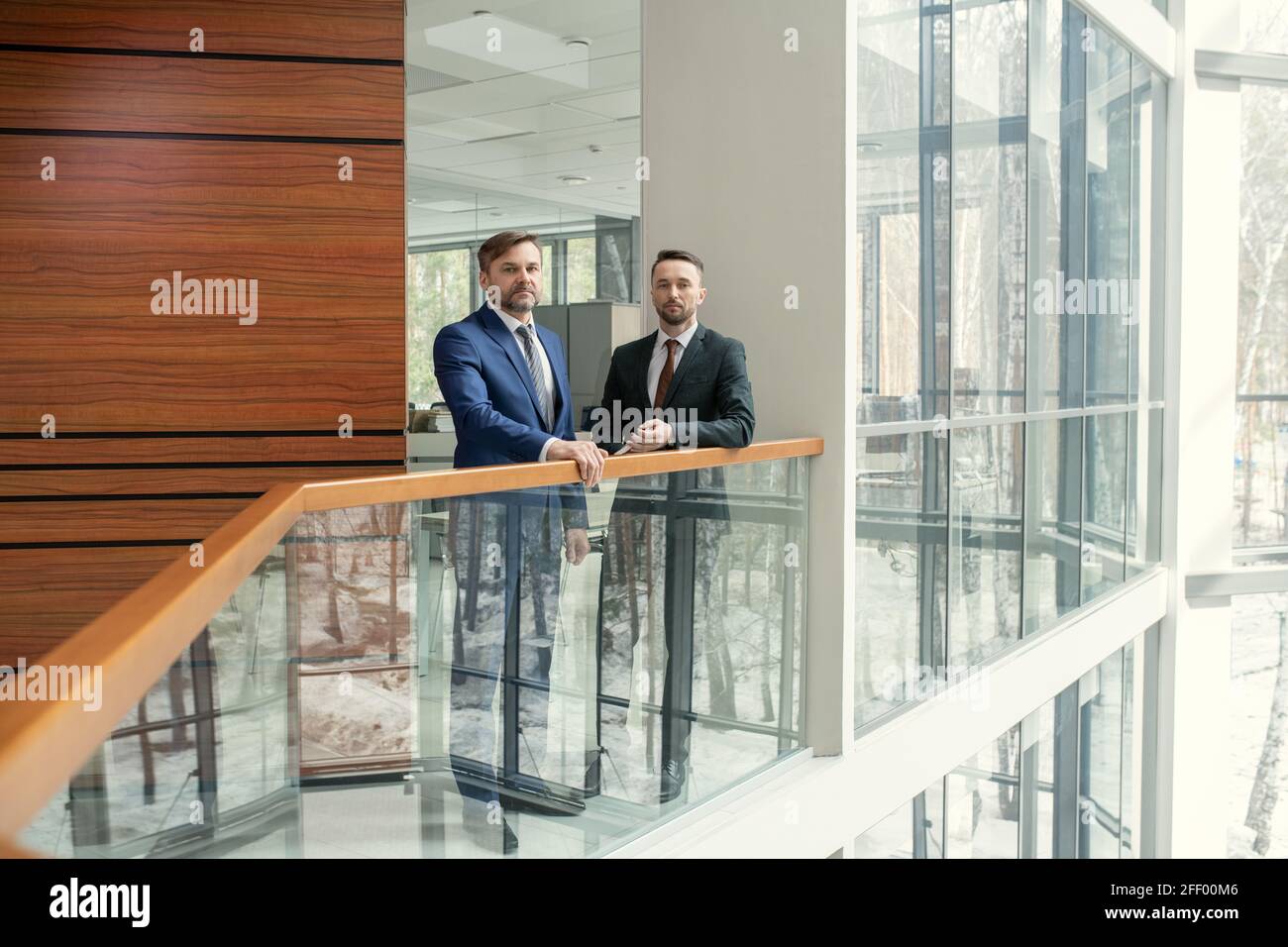 Ritratto di colleghi di lavoro sicuri in tute in piedi alla ringhiera e discutere di progetto in corridoio Foto Stock