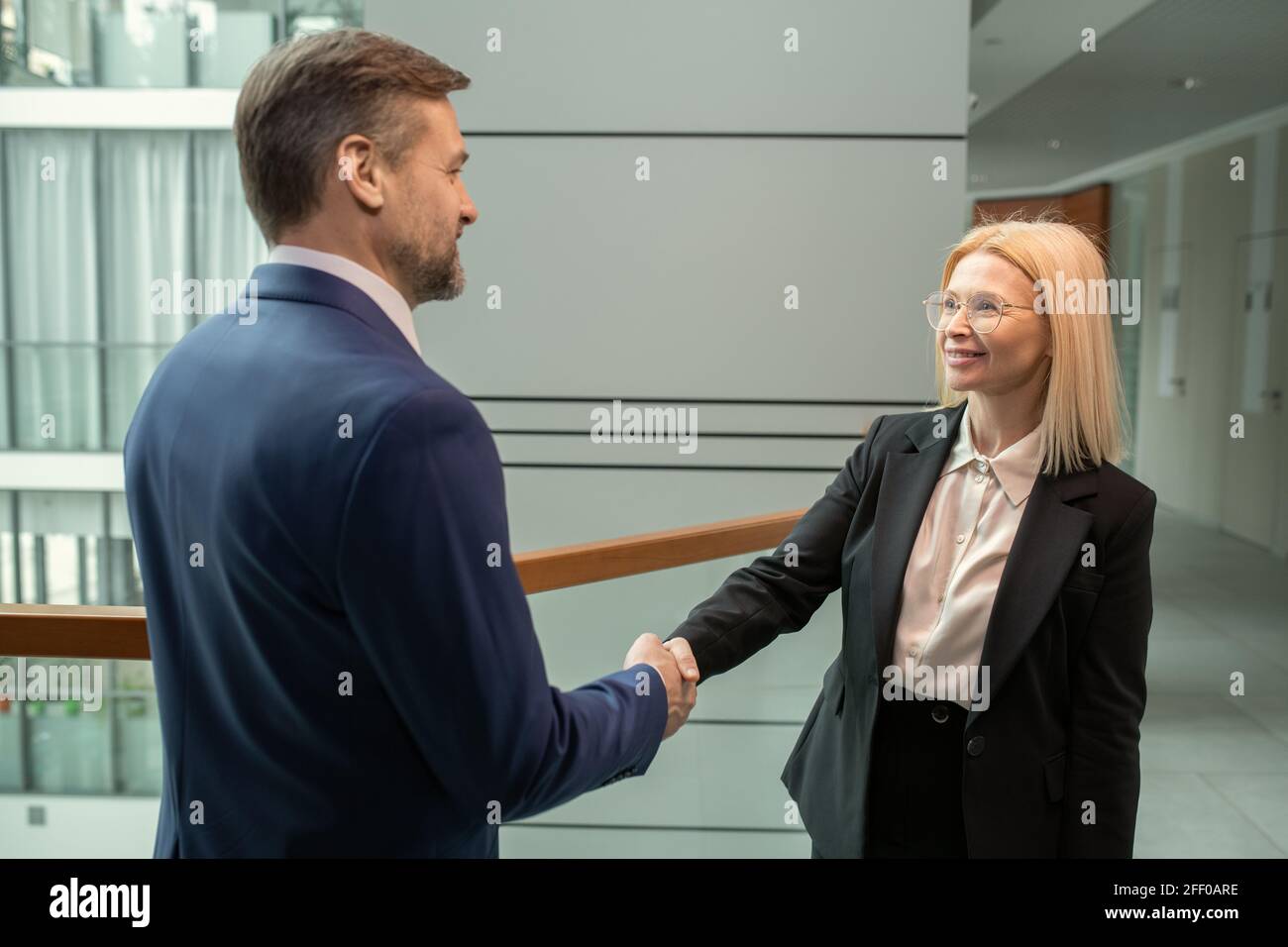 Sorridente imprenditore maturo attraente in occhiali facendo handshake con il commercio collaborate con lui nel business center Foto Stock