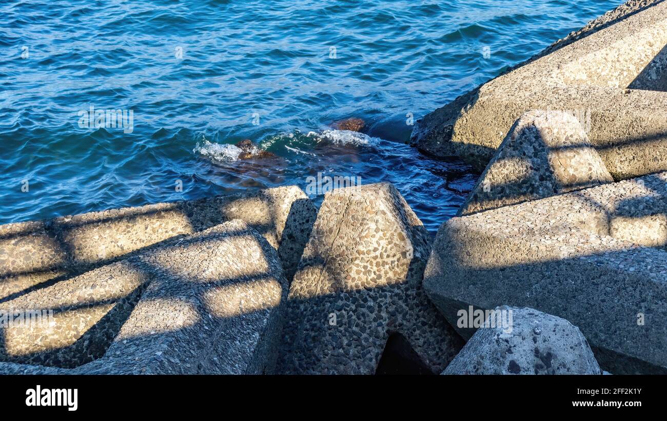 Le piccole onde si lavano dolcemente sopra i contorni di cemento, enormi, tetrapodi multi-ton, che si allineano intorno al 50% dell'area costiera del Giappone. Foto Stock