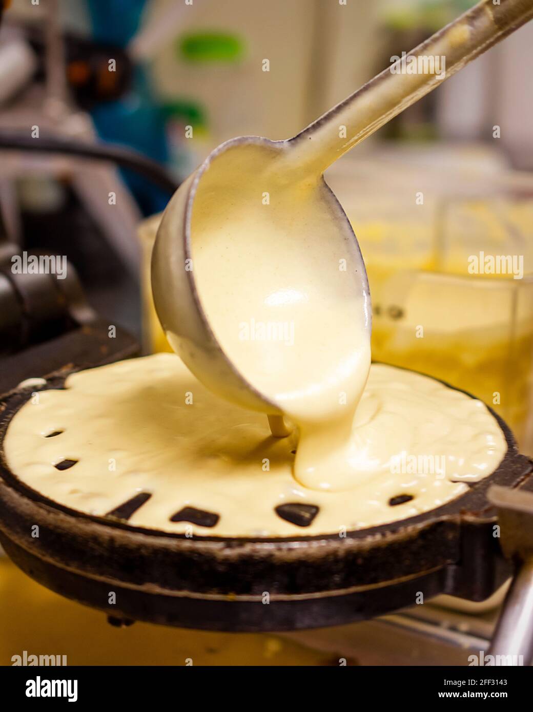 L'impasto dei waffle viene versato tramite siviera su waffle commerciali caldi in un ristorante. Foto Stock