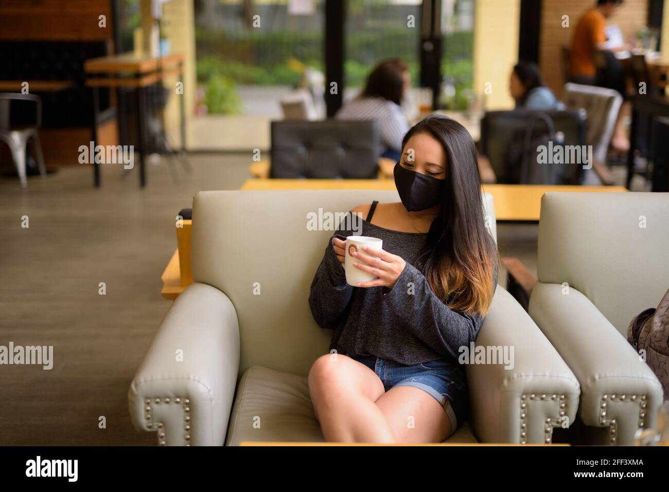 Donna che indossa maschera facciale per la protezione contro il coronavirus Covid-19 mentre seduto al bar Foto Stock