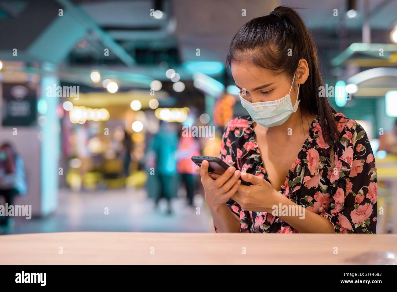 Ritratto di donna che indossa maschera per la protezione contro il coronavirus Covid-19 mentre si usa il telefono cellulare al ristorante Foto Stock