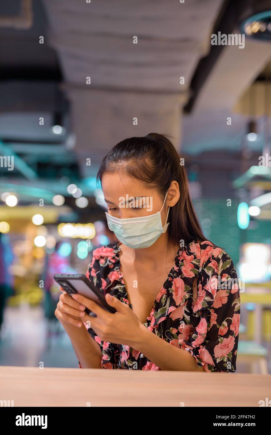Donna che indossa maschera facciale per la protezione contro il coronavirus Covid-19 mentre utilizzo del telefono cellulare al ristorante Foto Stock