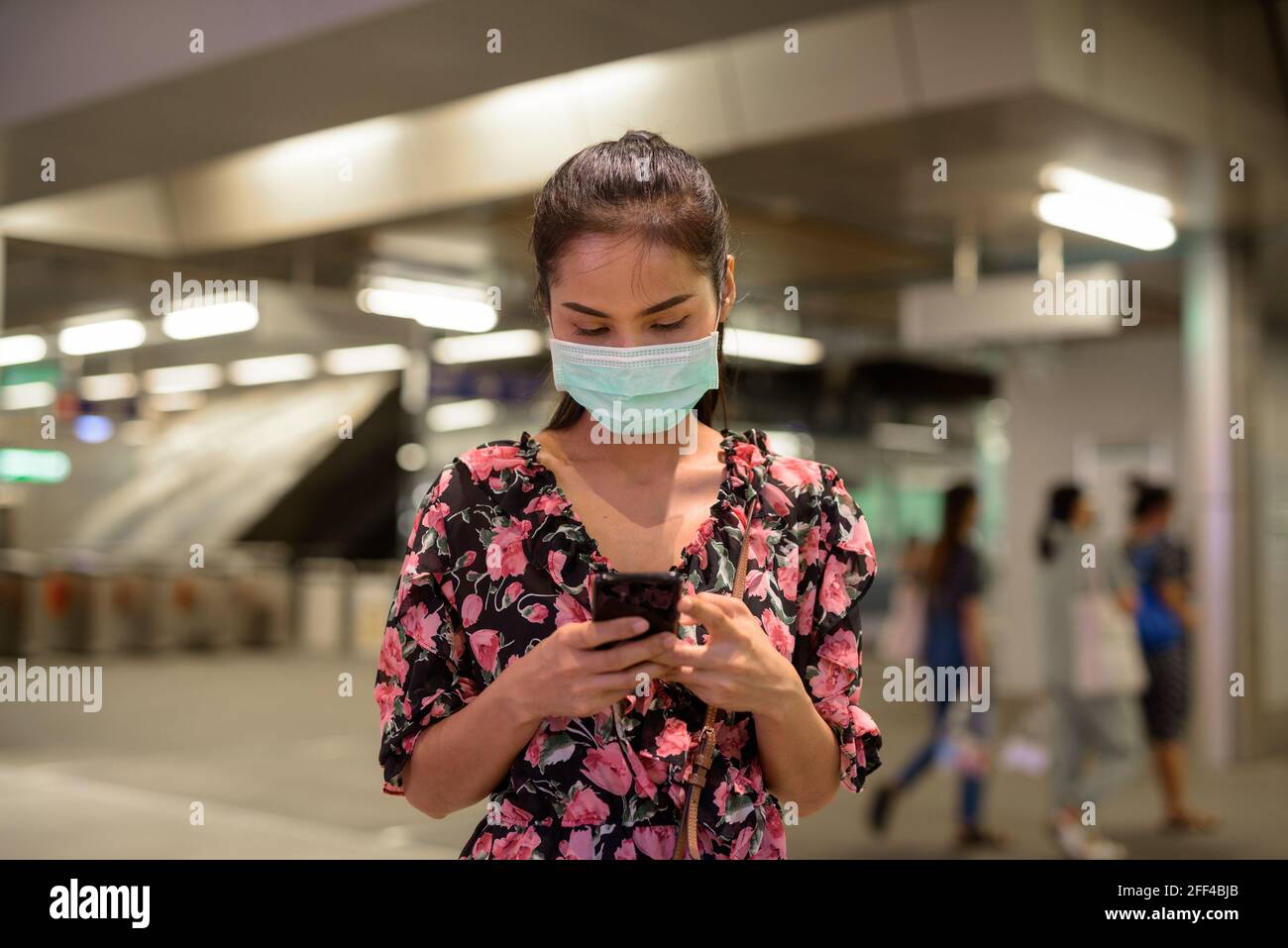 Donna che indossa maschera facciale per la protezione contro il coronavirus Covid-19 all'aperto di notte mentre si utilizza il telefono cellulare Foto Stock