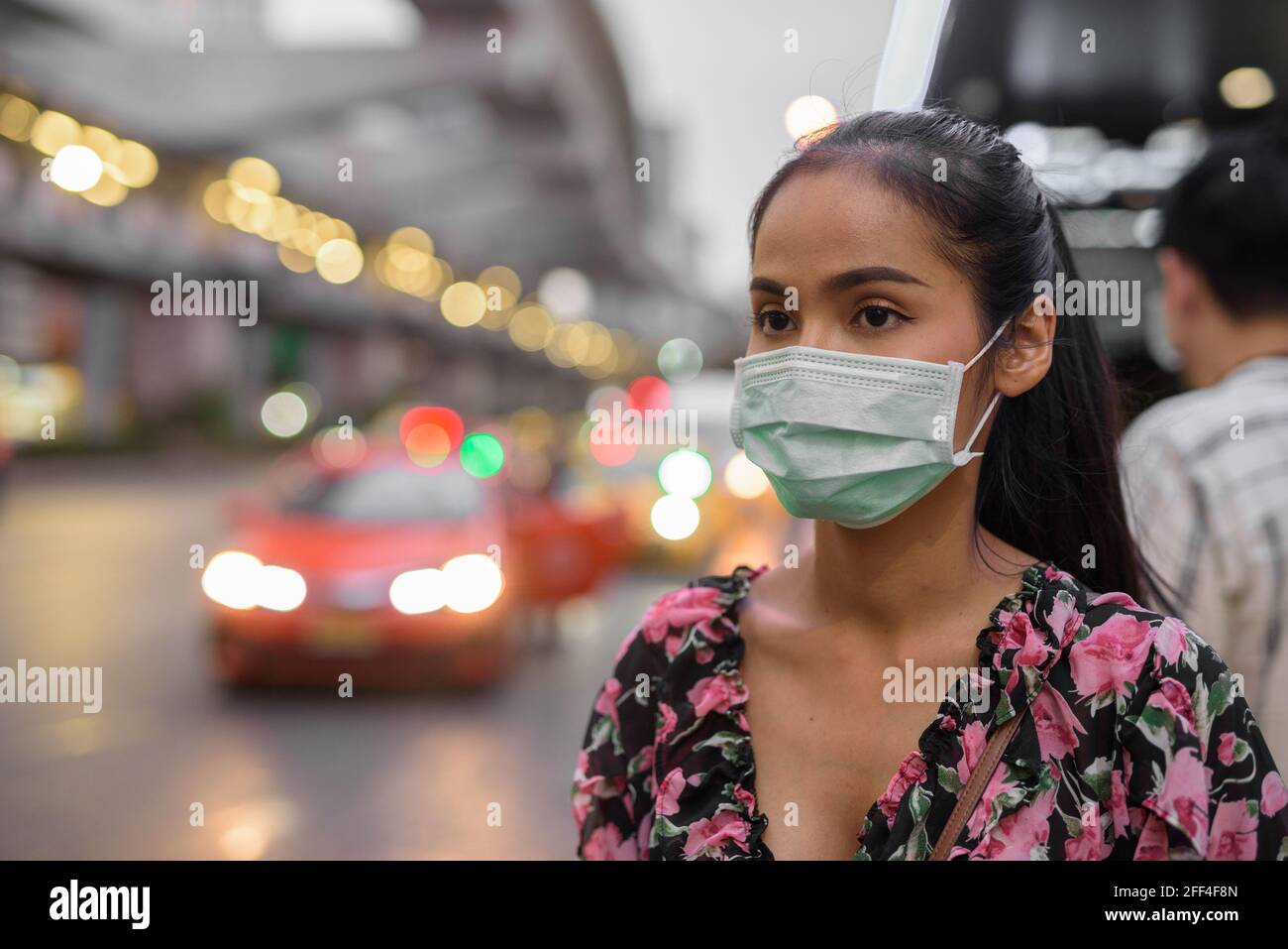 Donna che indossa maschera facciale per la protezione contro il coronavirus Covid-19 mentre attesa taxi di notte Foto Stock