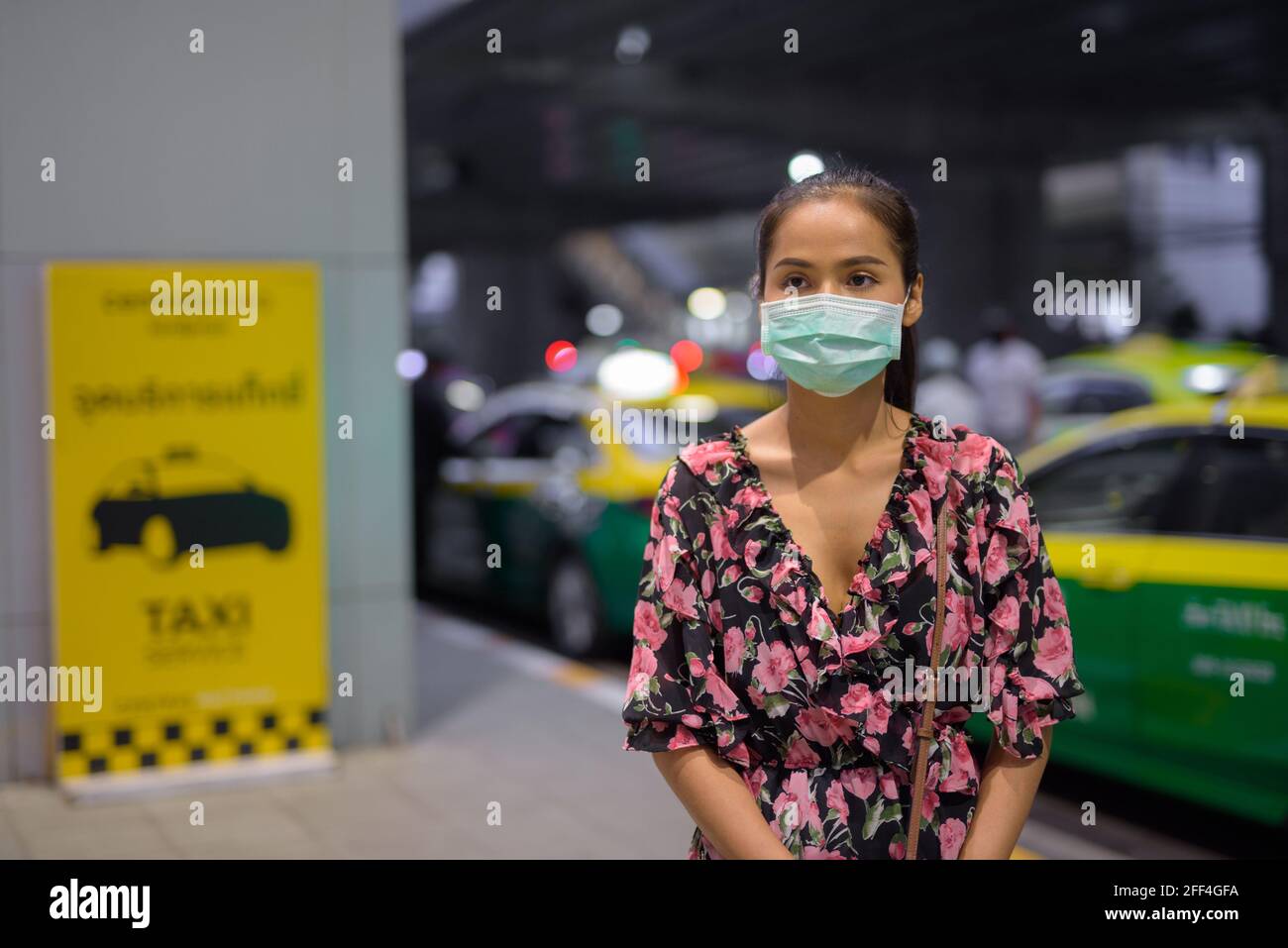 Donna che indossa maschera facciale per la protezione contro il coronavirus Covid-19 mentre attesa taxi di notte Foto Stock