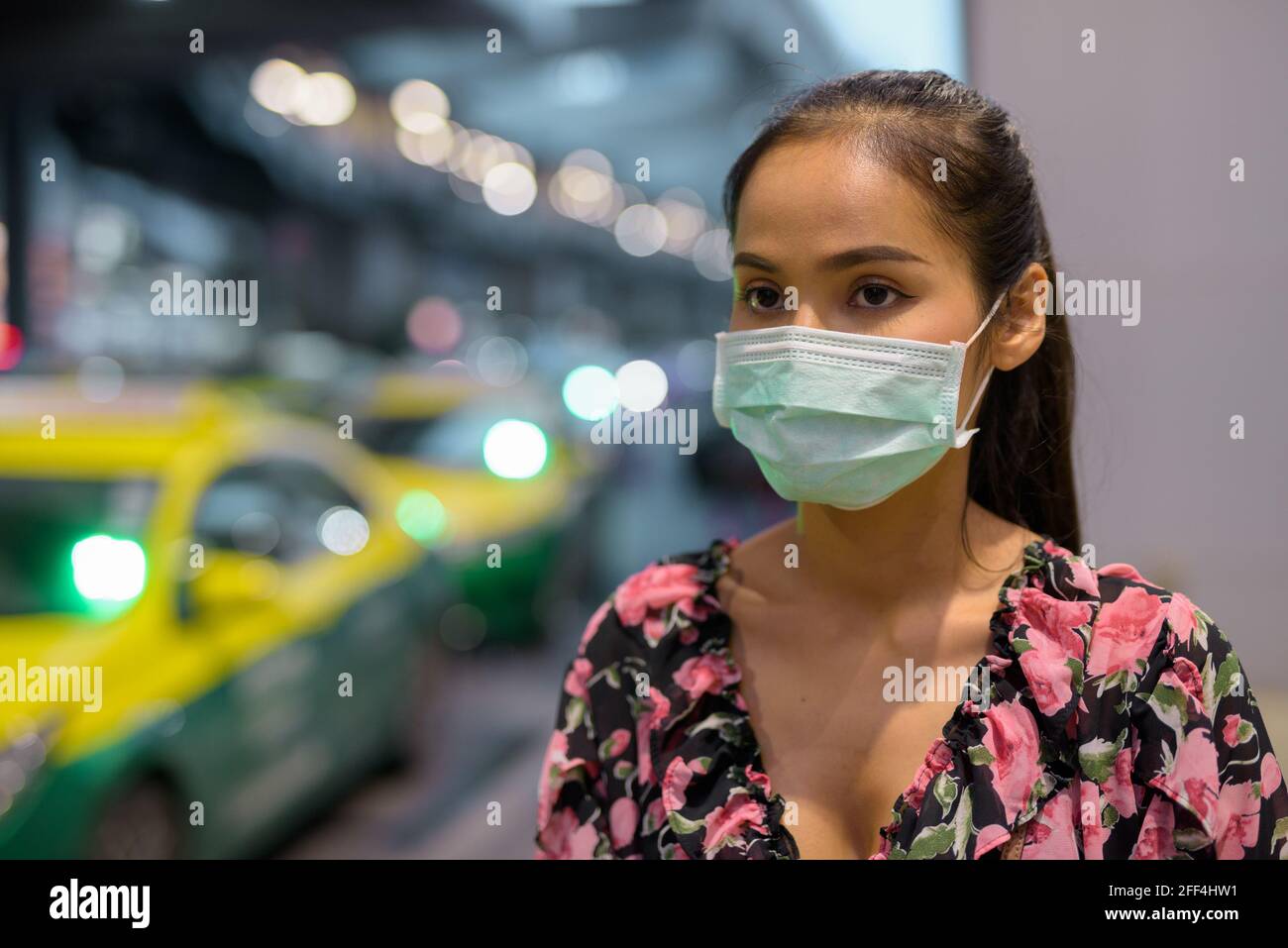 Donna che indossa maschera facciale per la protezione contro il coronavirus Covid-19 mentre attesa taxi di notte Foto Stock