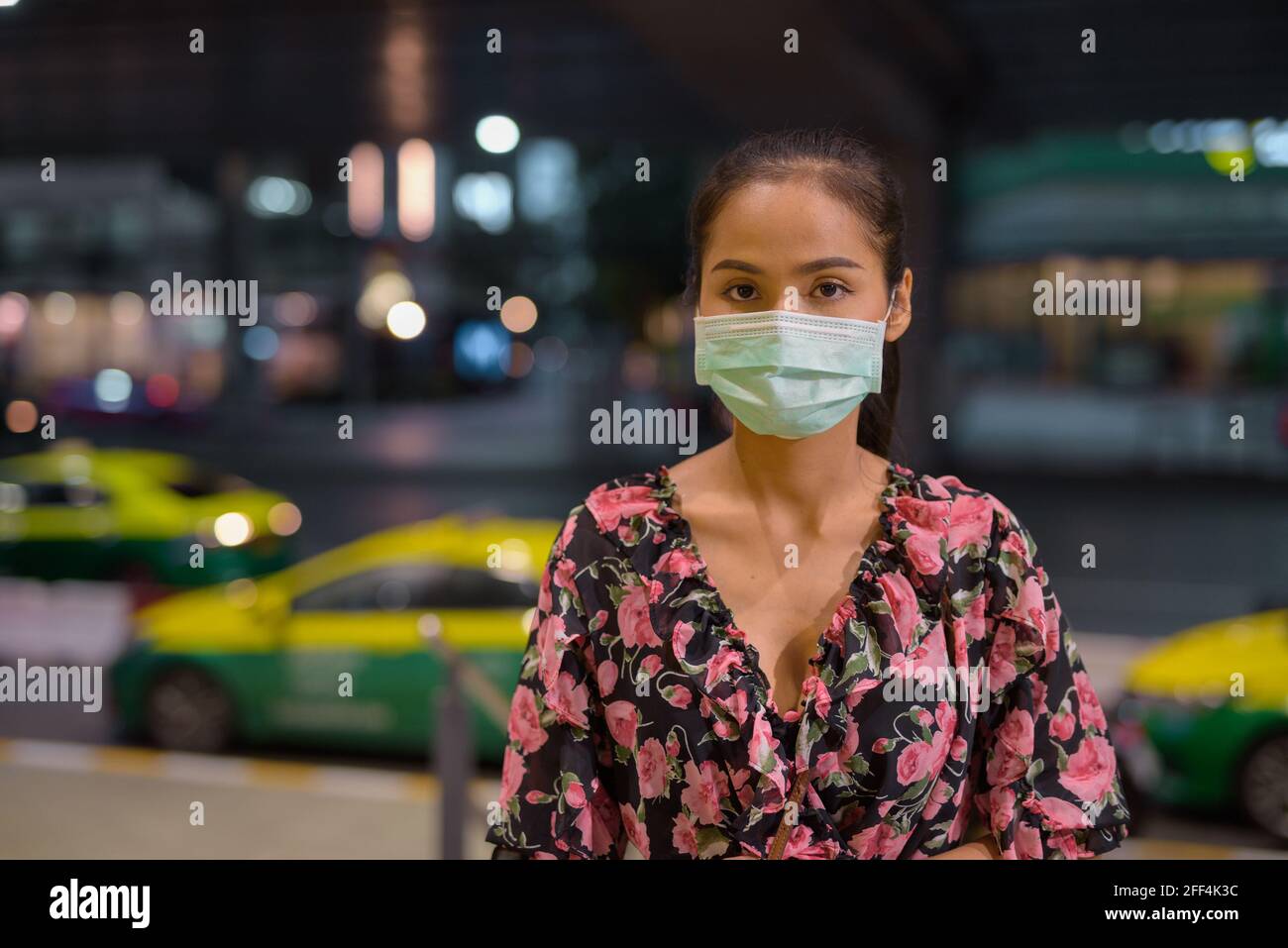 Donna che indossa maschera facciale per la protezione contro il coronavirus Covid-19 mentre attesa taxi di notte Foto Stock