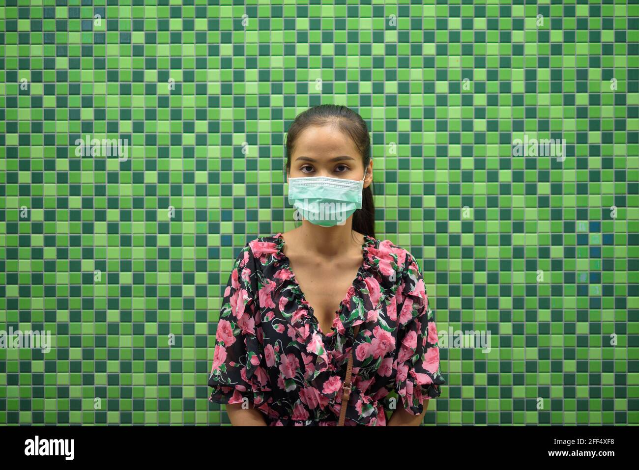 Ritratto di donna che indossa maschera per la protezione contro il coronavirus Covid-19 di notte contro parete colorata con spazio di copia Foto Stock