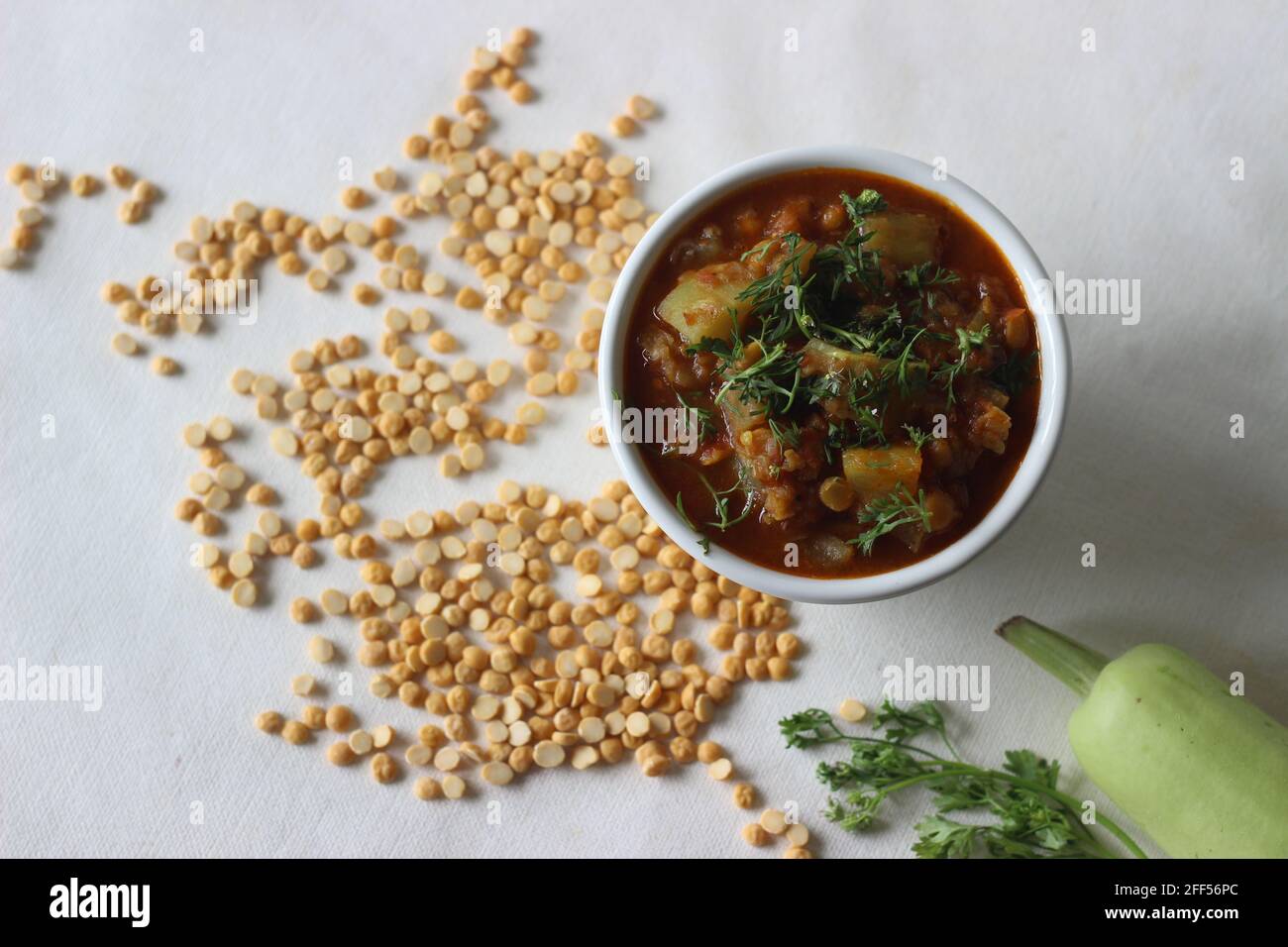 Una pentola di lenticchie di ceci cotte con una bottiglia di cipolle di zucca pomodori e spezie. Scatto su sfondo bianco. Foto Stock