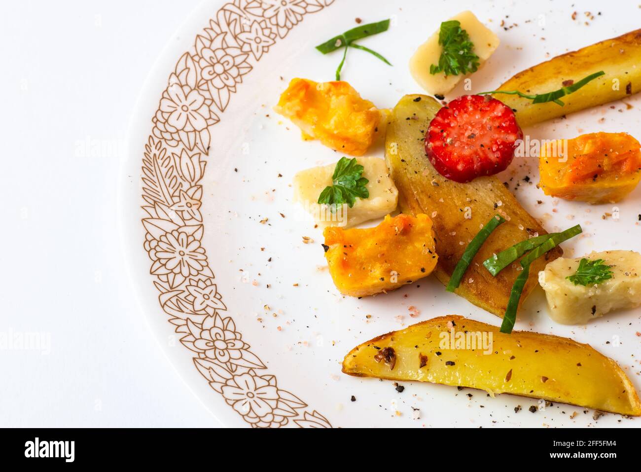 Pezzi di verdure arrosto (patate, sedano, zucchine) e purea con fragola cosparsa di pepe e erbe su tavola bianca, guardaroba. Foto Stock