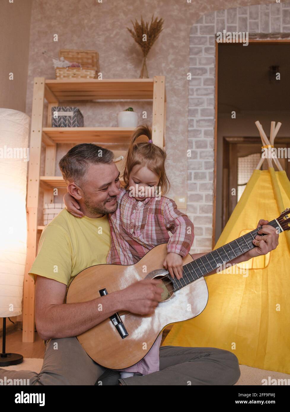 un padre felice suona la chitarra per la sua figlia piccola. cura ed  educazione dei bambini Foto stock - Alamy