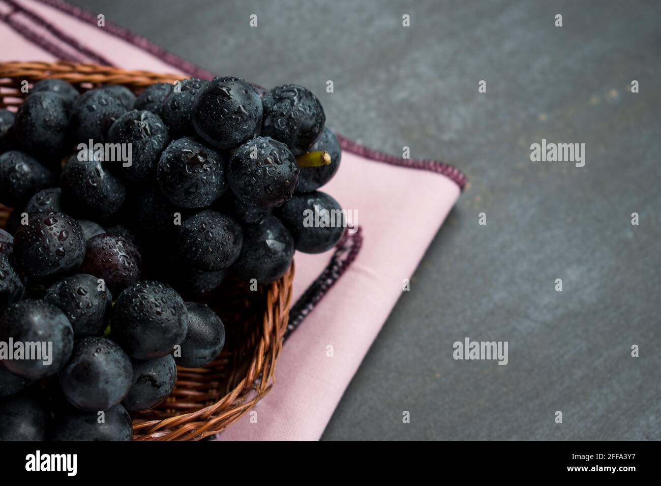Alcune uve in un cesti su un tavolo nero con tovaglia rosa Foto Stock