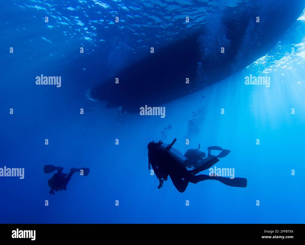 I subacquei tornano in barca sott'acqua con la barca sulla superficie in silhouette e raggi di luce che penetrano dall'alto. Foto Stock