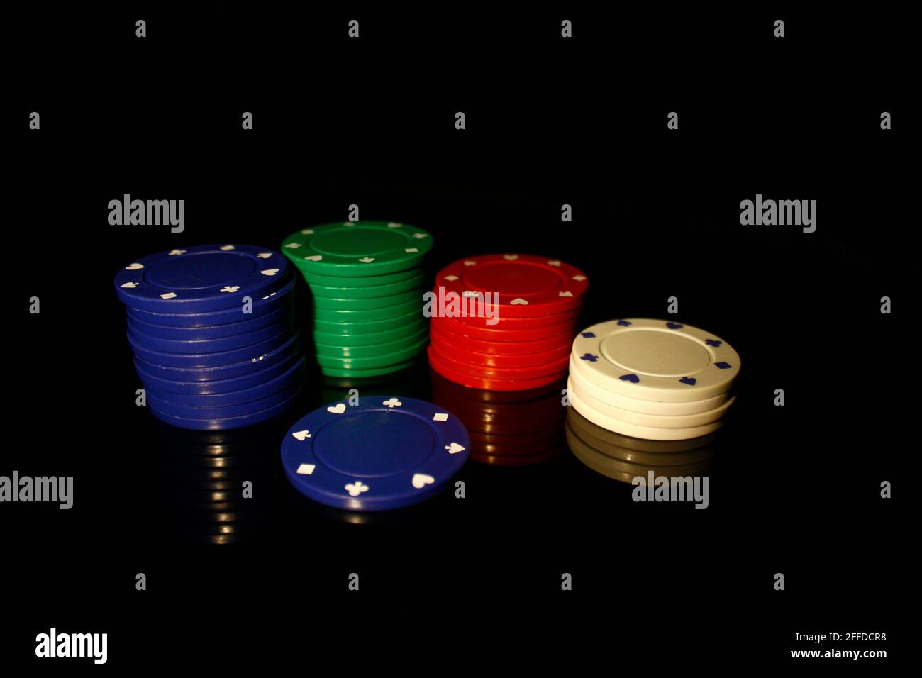 Quattro colori chip casinò stack con un chip bianco di fronte, isolato su nero con riflessione Foto Stock