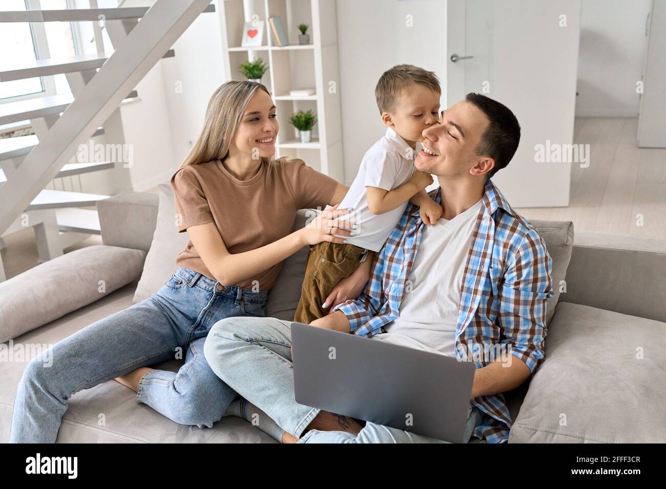Felice giovane coppia con bambino seduto sul divano a casa utilizzando il computer portatile. Foto Stock