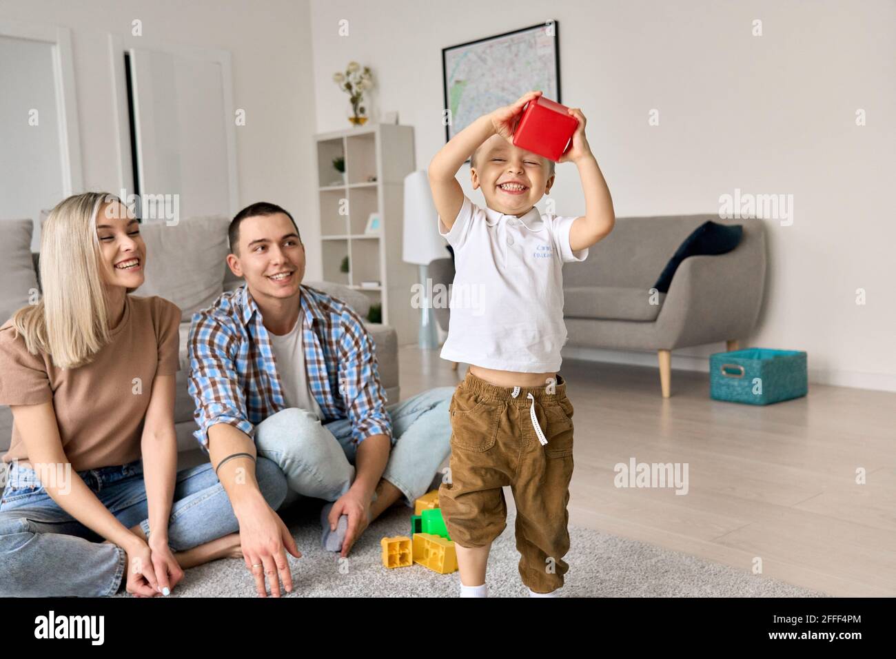 Felice giovane famiglia con bambino a casa seduto sul pavimento godendo del tempo insieme. Foto Stock