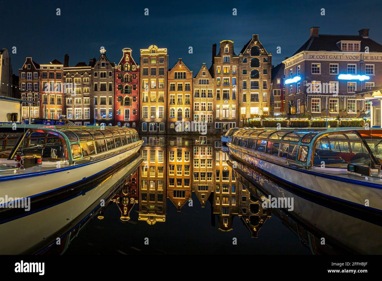 Amsterdam Damrak architettura tradizionale olandese di notte. Tour delle navi da crociera in primo piano. Foto Stock