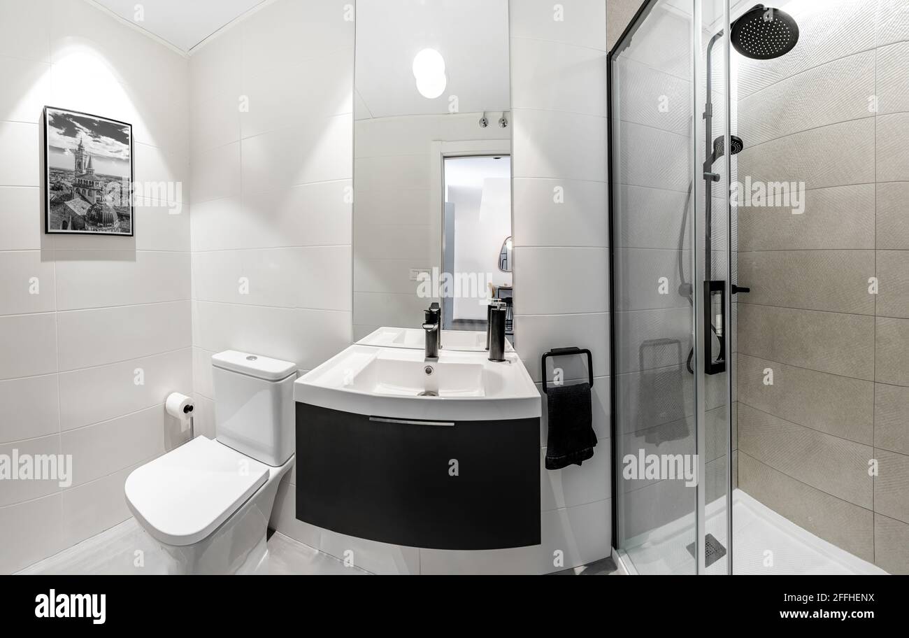 Panorama di un bagno pulito e luminoso interno con rubinetto nero opaco e piastrelle bianche. Spazio dal design originale con mobili e pezzi moderni Foto Stock