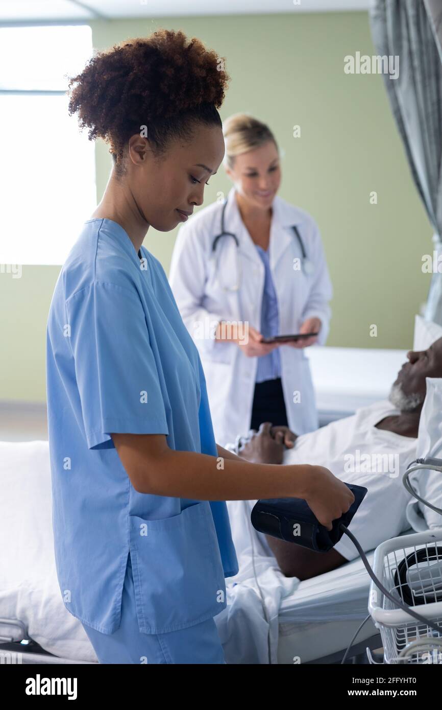 Razza mista dottoressa in camera paziente che si prepara al controllo pressione sanguigna del paziente maschile Foto Stock