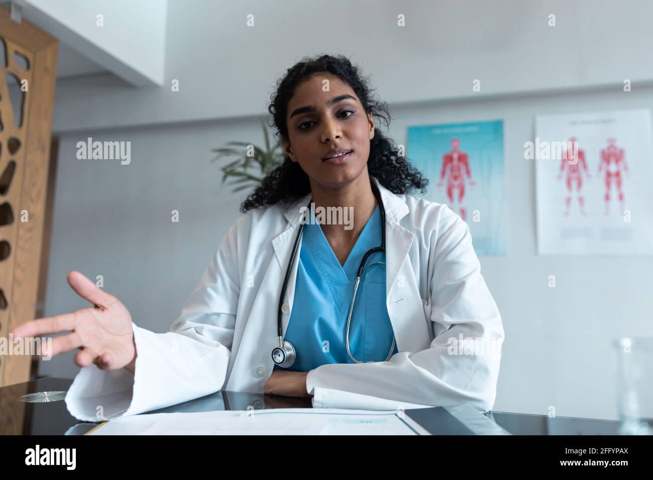 Razza mista dottoressa alla scrivania parlare e gesturing durante consultazione videochiamata Foto Stock