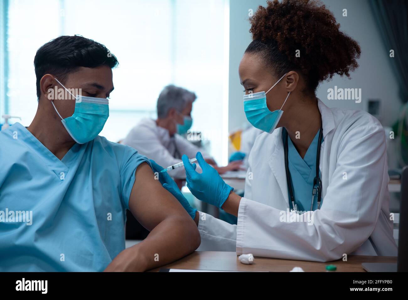 Razza mista coppia di medici che indossano maschere facciali facendo l'iniezione Foto Stock