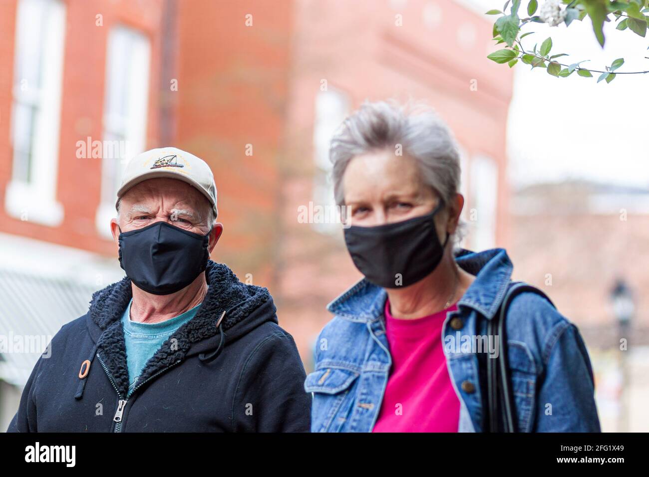 Easton, MD, USA 04-16-2021: Una coppia caucasica anziana che indossa abiti casual, cappello e maschera di stoffa sta camminando per strada durante COVID-19 pande Foto Stock