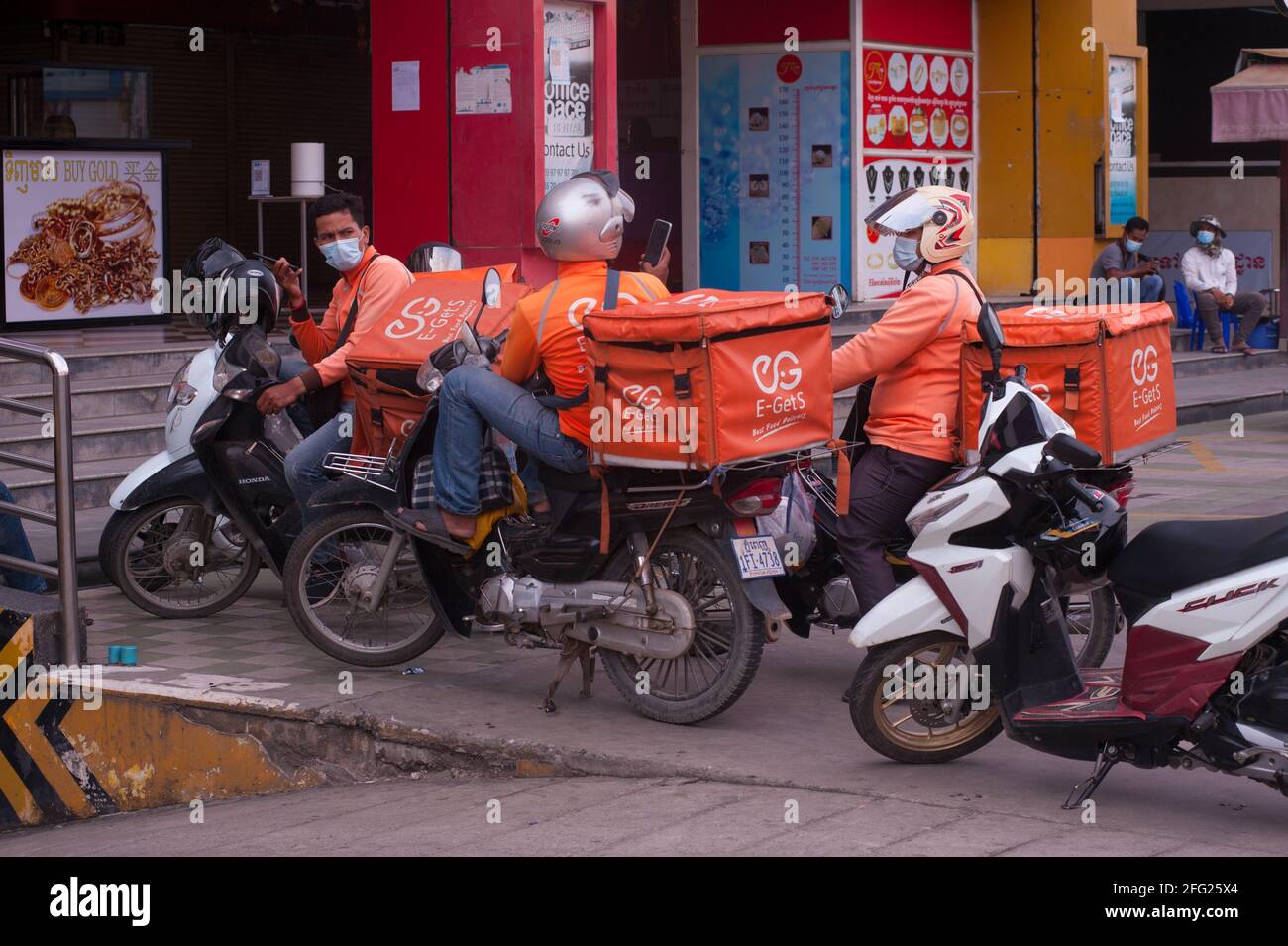 A causa di un recente focolaio di COVID-19 nei mercati e nelle fabbriche di abbigliamento, Il governo cambogiano ha imposto un blocco. Qui i conducenti di consegna di cibo sulle motociclette hanno un incontro improvvisato su come ottenere il loro cibo attraverso i posti di controllo della polizia e blocchi stradali. Molti cambogiani sono in quarantena e non sono autorizzati a lasciare la loro strada per fare shopping durante la pandemia del coronavirus. Stueng Meanchey, Phnom Penh, Cambogia. 15 aprile 2021. © Kraig Lieb Foto Stock