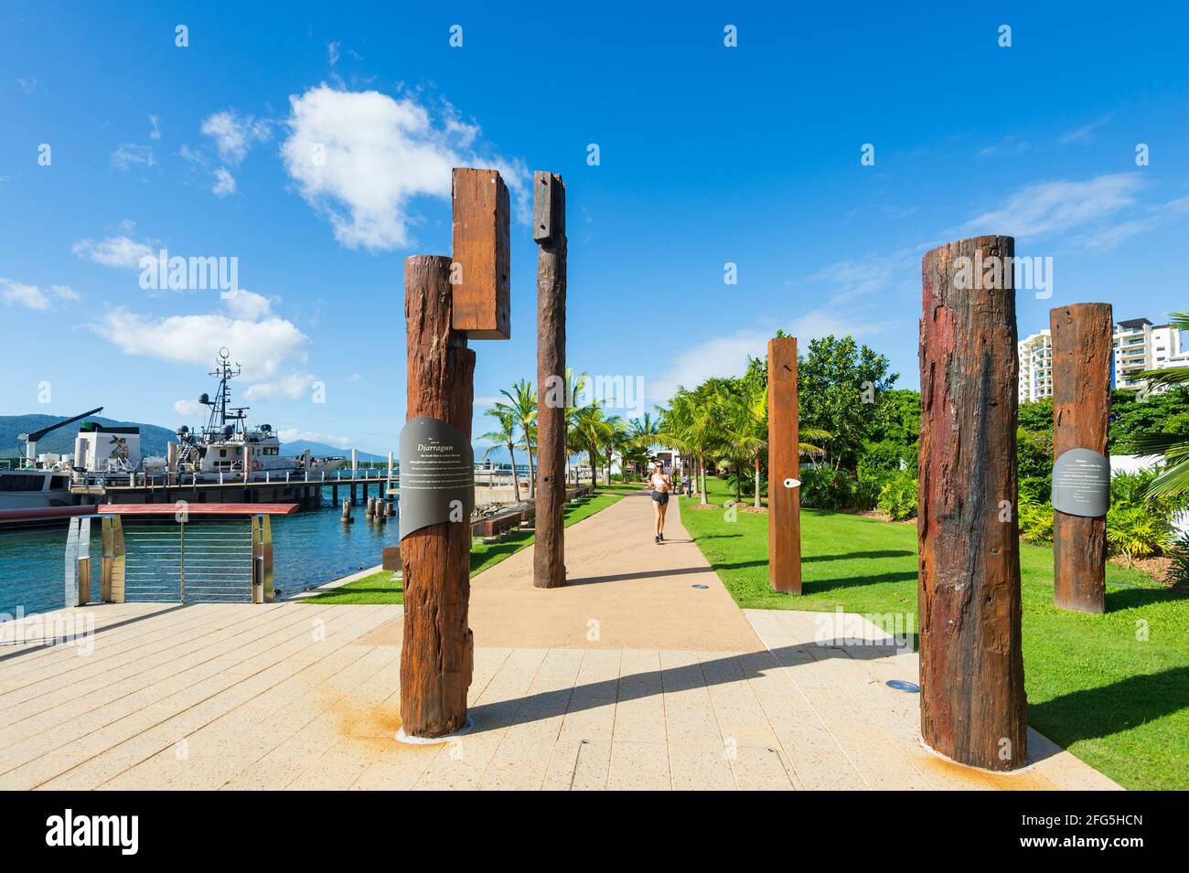 Giovane femmina che fa jogging dopo un'installazione di arte pubblica di totem sul litorale di Trinity Inlet, Cairns, far North Queensland, FNQ, QLD, Australia Foto Stock