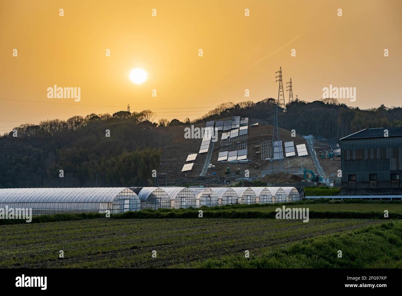Il sole si fissa su pannelli solari e serre Foto Stock