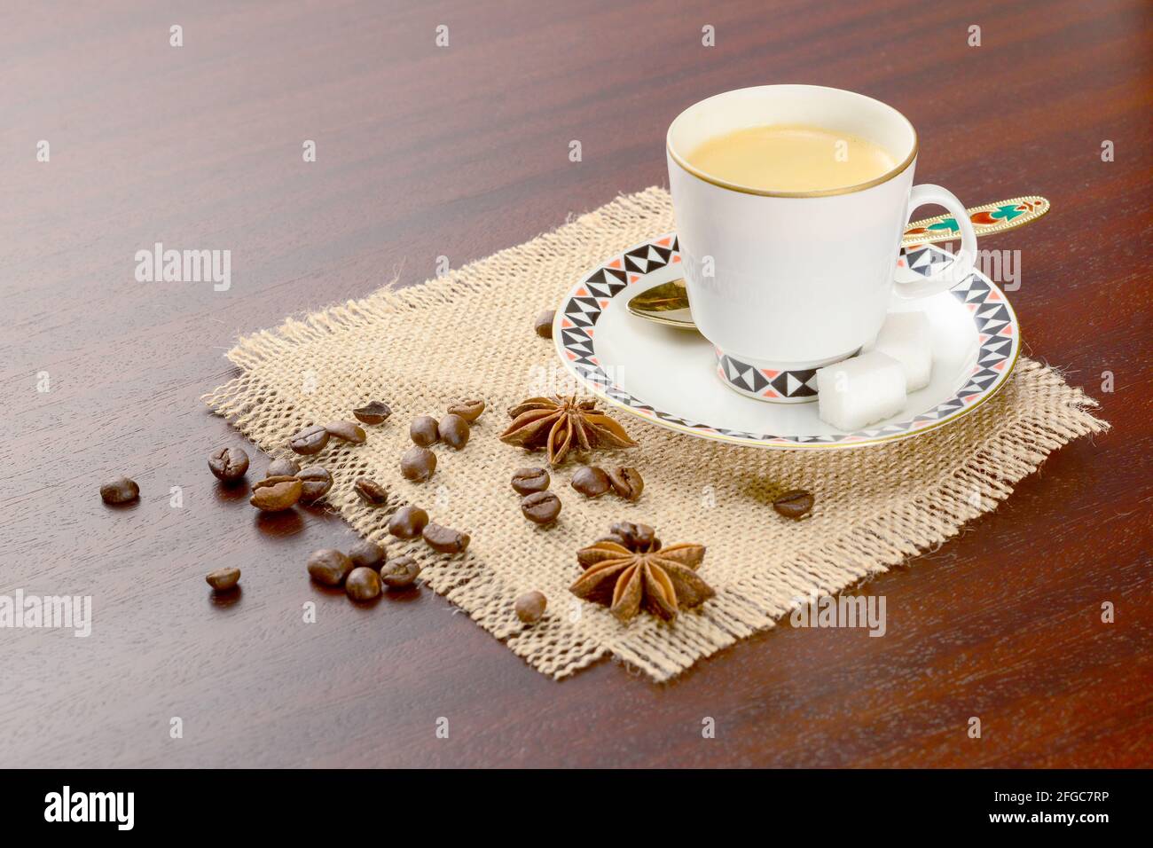 Caffè in tazza di porcellana con piattino e chicchi di caffè con anice stellato. Caffè vintage su tavolo di legno, con zucchero e chicchi di caffè Foto Stock