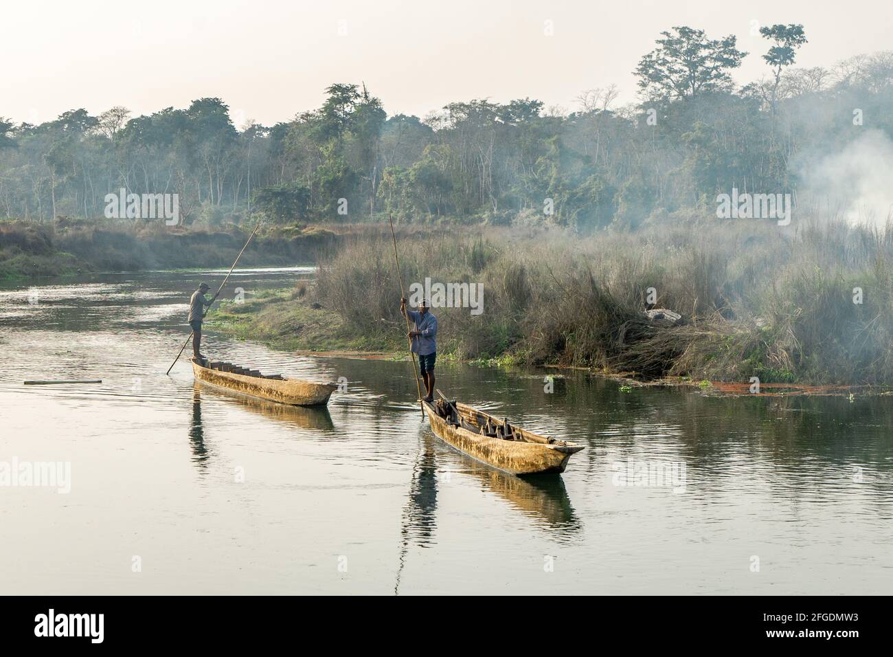 Due uomini spingono canoe o barche lungo il fiume nel Parco Nazionale di Chitwan, Nepal Foto Stock