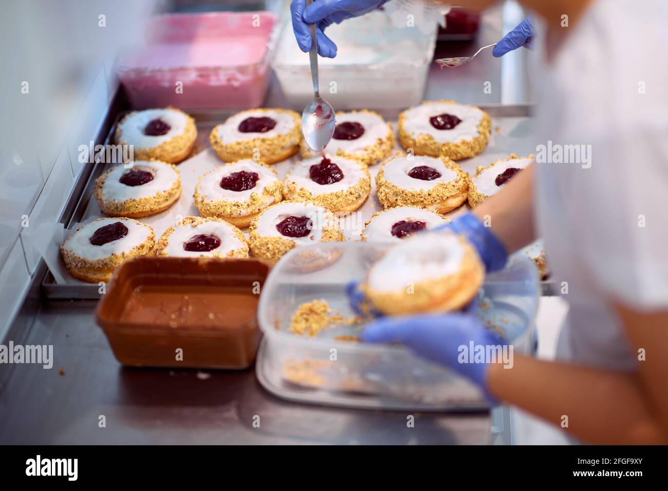 I lavoratori riempiono deliziose ciambelle di marmellata in un'atmosfera di lavoro in un laboratorio di caramelle. Pasticceria, dessert, dolce, fare Foto Stock