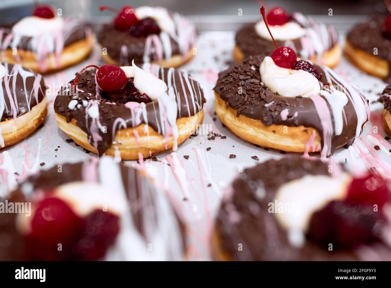 Deliziose ciambelle dall'aspetto irresistibile con condimento al cioccolato e ciliegia sulla parte superiore del vassoio pronto per una pasticceria. Pasticceria, dessert, dolce Foto Stock