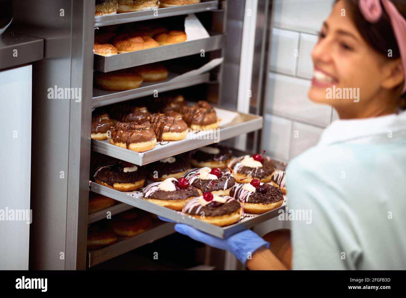 Una giovane piccola impresa donna proprietario in un'atmosfera piacevole in un laboratorio caramelle riempie l'armadio con deliziose ciambelle fatte a mano con soddisfazione. PA Foto Stock