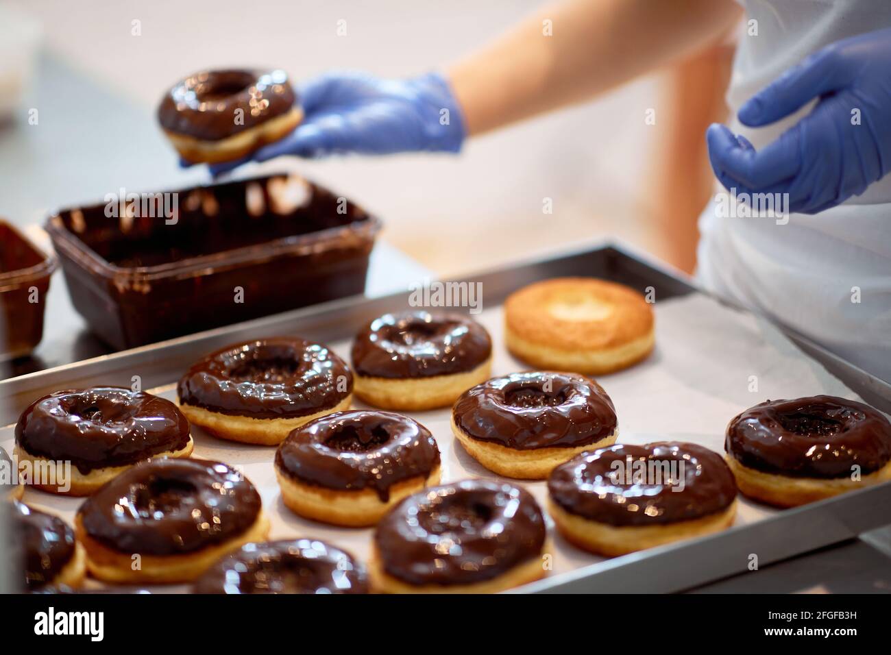 Condimento di cioccolato su ciambelle in un'atmosfera di lavoro in un laboratorio di caramelle. Pasticceria, dessert, dolce, fare Foto Stock