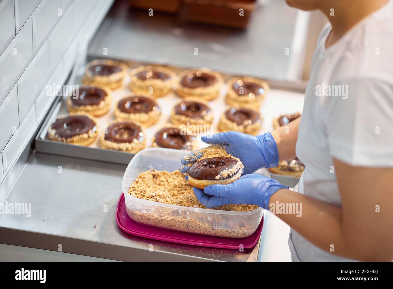 Un lavoratore che fa le ciambelle deliziose in un'atmosfera di lavoro in un laboratorio di caramelle. Pasticceria, dessert, dolce, fare Foto Stock