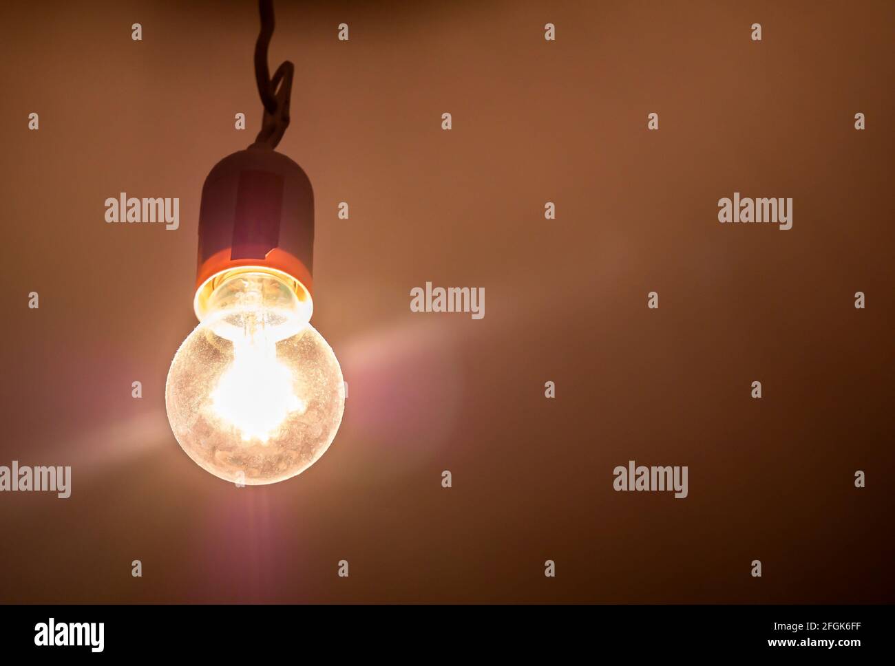 Una vecchia vecchia vecchia lampadina ad incandescenza luminosa in una stanza buia, dettaglio dell'oggetto, primo piano, da sotto una sorgente luminosa gialla luminosa illumina il suo Foto Stock