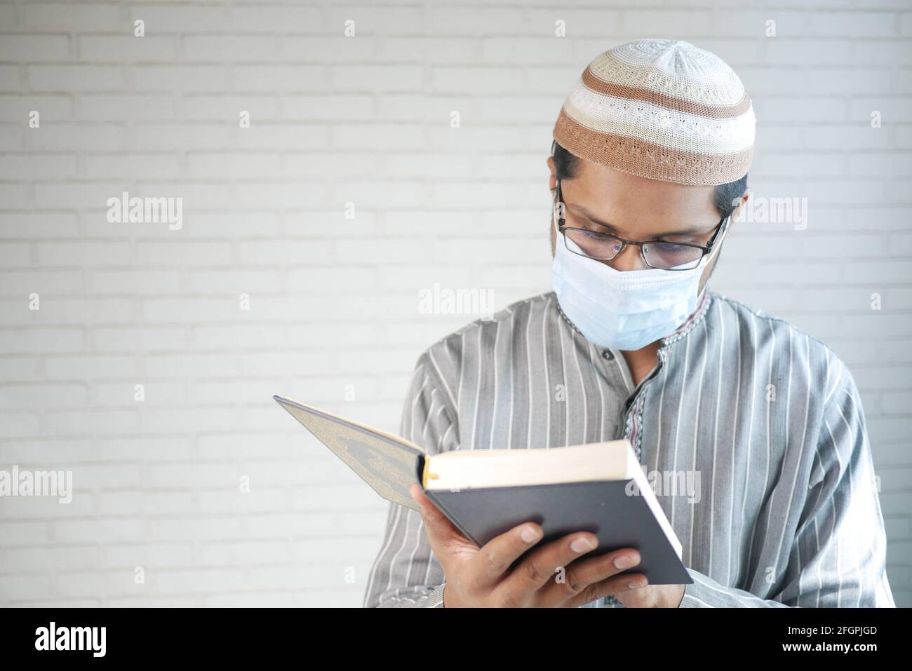 uomo musulmano con maschera di lettura del libro sacro di quran interno Foto Stock