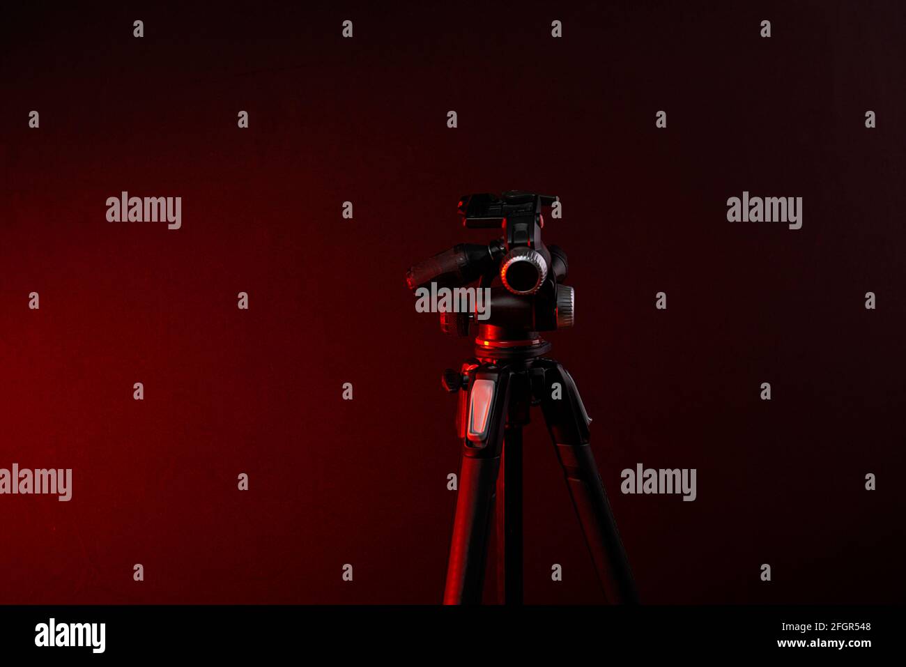 Treppiede per fotocamera isolato su sfondo studio rosso scuro chiaro Foto Stock