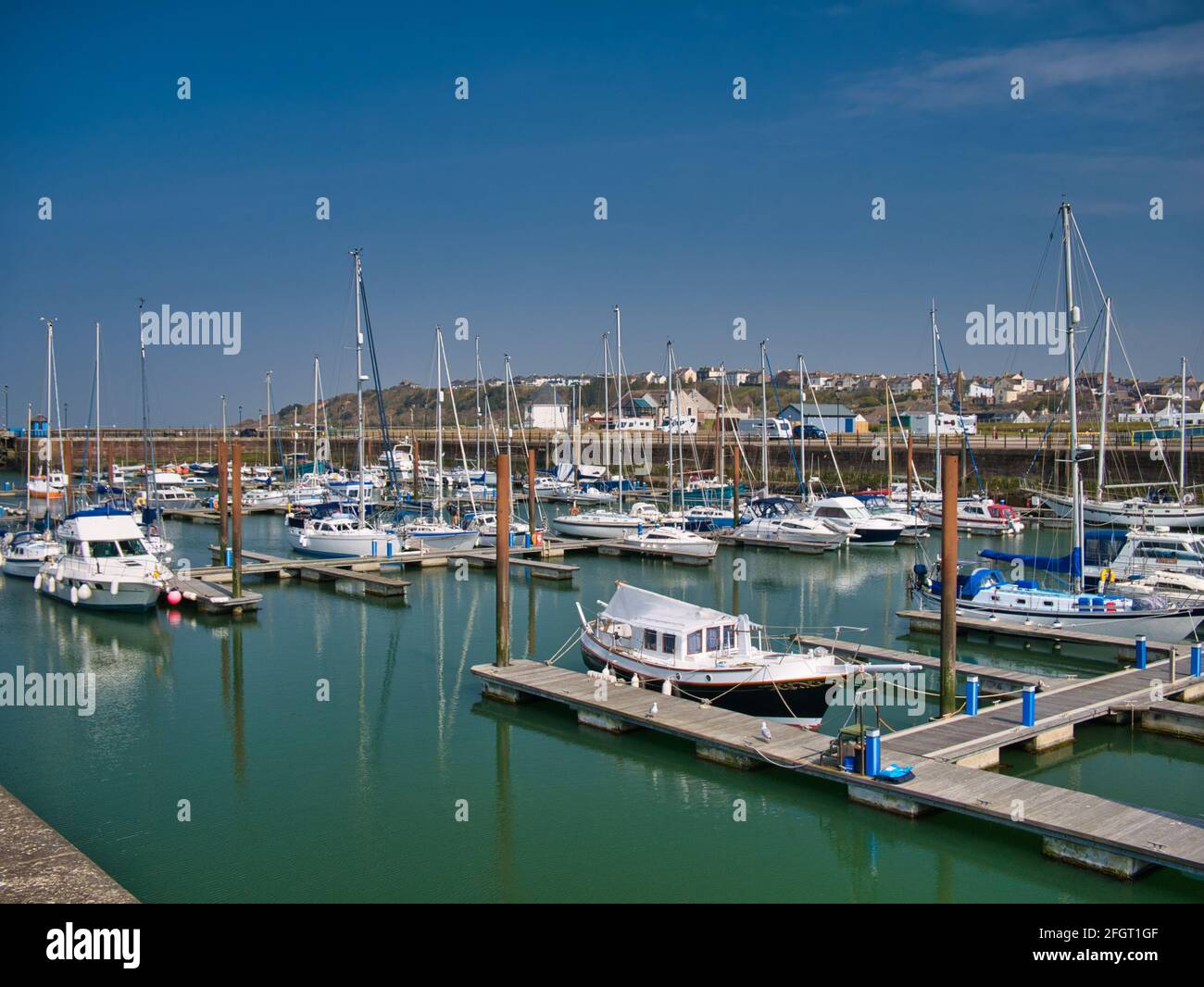 Al sole in una tranquilla giornata di sole, le barche per il tempo libero ormeggiate sui moli di Maryport Marina nel nord-ovest di Cumbria, Inghilterra, Regno Unito. Nelle acque calme sono il riflesso Foto Stock